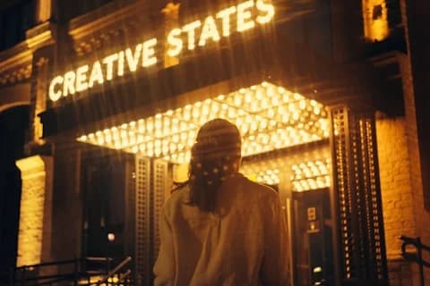 Person under a glowing Creative States marquee at night